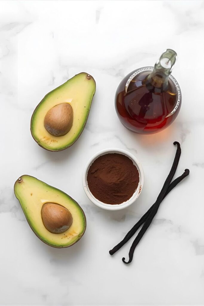 A flat-lay image of the ingredients for avocado chocolate mousse, including avocados, cocoa powder, and maple syrup.