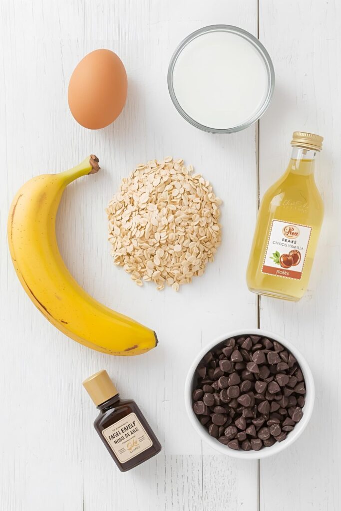 A clean and organized flat lay of ingredients for baked oats on a light wooden background. A small pile of rolled oats, a ripe banana, a brown egg, a glass of milk, a small bottle of vanilla, and a bowl of chocolate chips are arranged neatly. The scene is bright and inviti