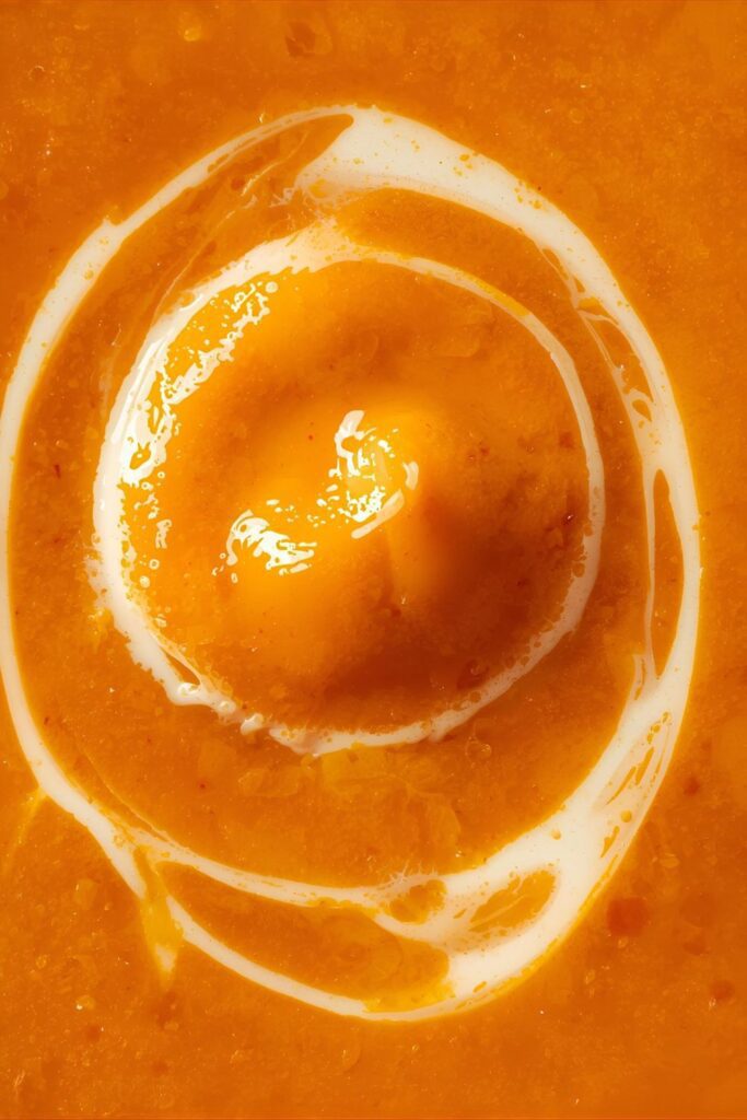  An extreme close-up, top-down shot of the soup, focusing on its velvety, smooth texture and a swirl of cream.
