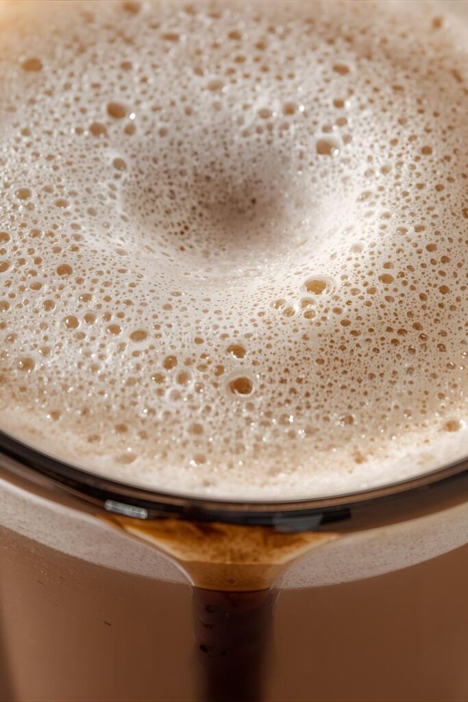 An extreme close-up shot focusing on the smooth, velvety microfoam and rich color of the mocha, with melted chocolate visible at the bottom of the glass.