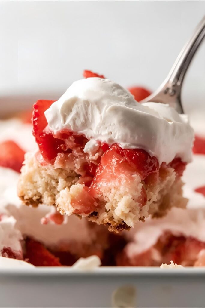 A close-up shot of a spoon scooping into a layered no-bake strawberry shortcake, showing the creamy texture.