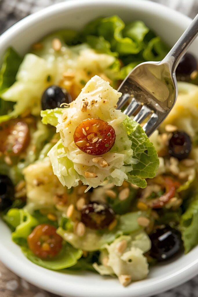 A close-up, mouth-watering shot of a single serving of Olive Garden salad in a white bowl, showing the crisp texture of the lettuce, the glistening dressing, and clearly visible toppings like black olives and pepperoncini, with a fork ready to pick up a bite. `