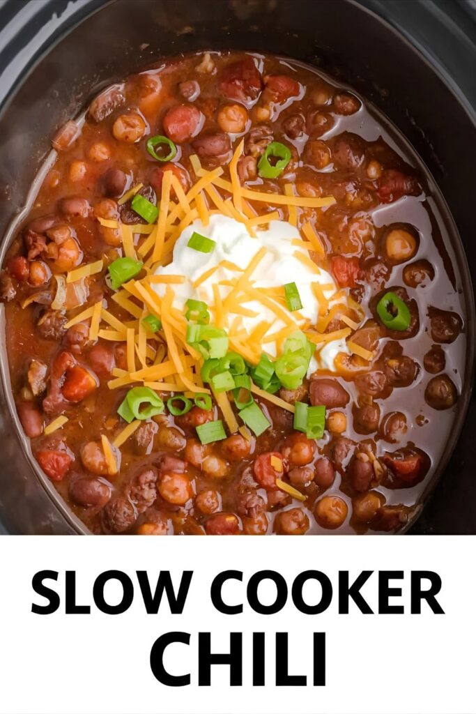 Overhead view of a slow cooker with bubbling chili, garnished with sour cream, cheese, and green onions, with the text overlay "SLOW COOKER CHILI".