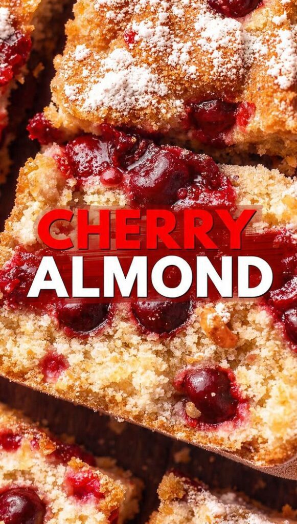 A close-up, vibrant overhead photo of a freshly baked cherry almond cake slice showing the moist interior and bright red cherries, featuring the bold text overlay: CHERRY ALMOND.