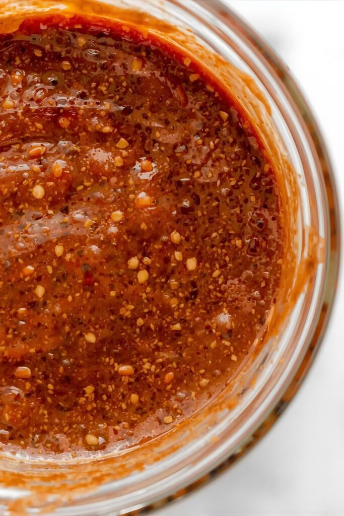 A side-by-side photograph showing two finished meats glazed with the sauce: On the left, smoked pulled pork coated in the classic Coffee BBQ Sauce; on the right, chicken wings coated in the thick, glossy Spicy Chipotle Coffee BBQ Sauce.