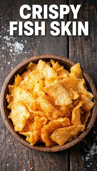A pile of golden-brown, thin, and brittle crispy fish skin chips stacked in a rustic bowl, dusted with sea salt. Text overlay reads: CRISPY FISH SKIN