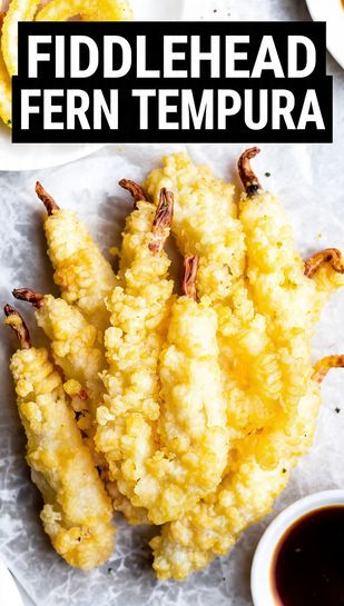 A pile of perfectly golden-brown, crispy fiddlehead fern tempura pieces on a plate, with a small bowl of dipping sauce on the side. Text overlay reads: FIDDLEHEAD FERN TEMPURA