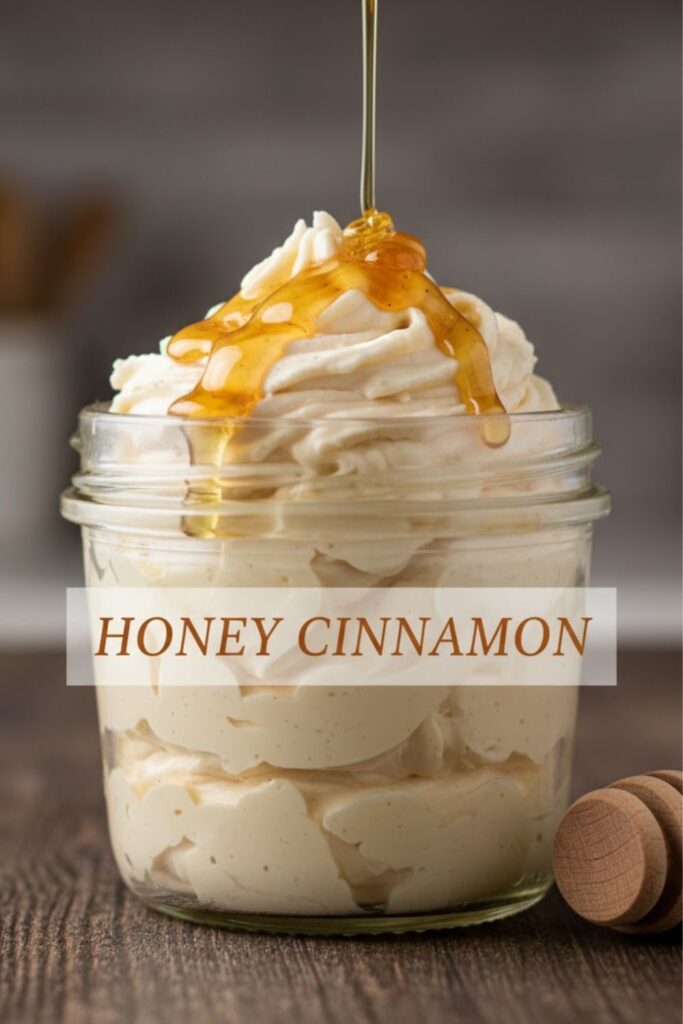A close-up, high-angle shot of light, airy, creamy Honey cinnamon butter swirled high in a small glass or rustic bowl, with a drizzle of honey pouring over the top. The text overlay reads: HONEY CINNAMON
