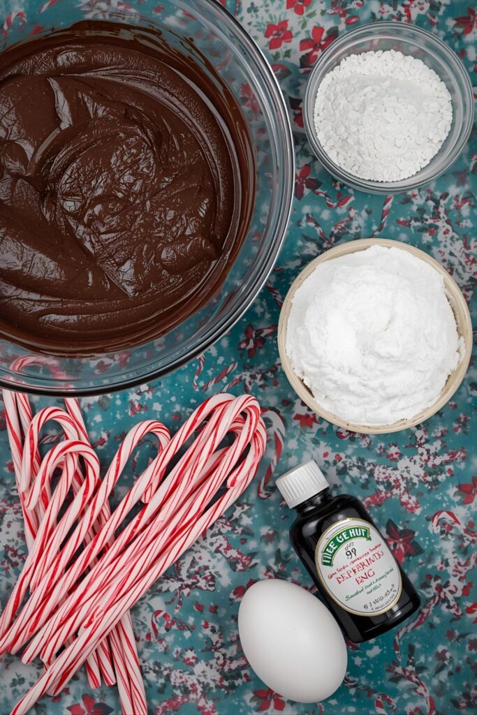 A flat-lay collage of the main ingredients for peppermint brownies: melted chocolate, powdered sugar, eggs, a bottle of peppermint extract, and a handful of candy canes on a festive background.
