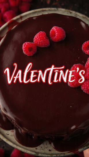 A close-up, vibrant overhead photo of a rich red wine chocolate cake covered in dark chocolate ganache, garnished with fresh raspberries, featuring the bold text overlay: VALENTINE'S.
