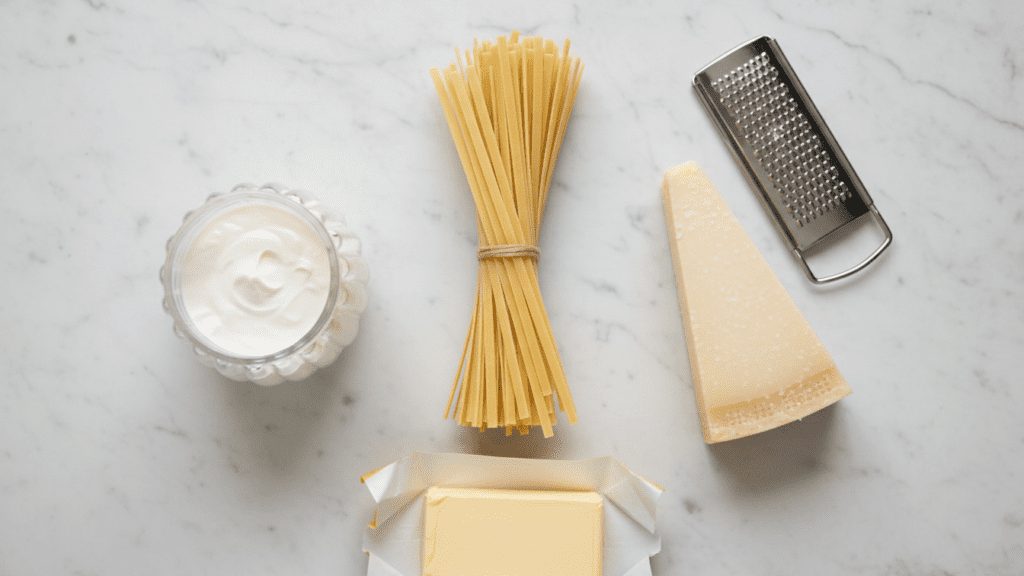 A collage of ingredients including fettuccine, heavy cream, a block of parmesan, and a stick of butter.