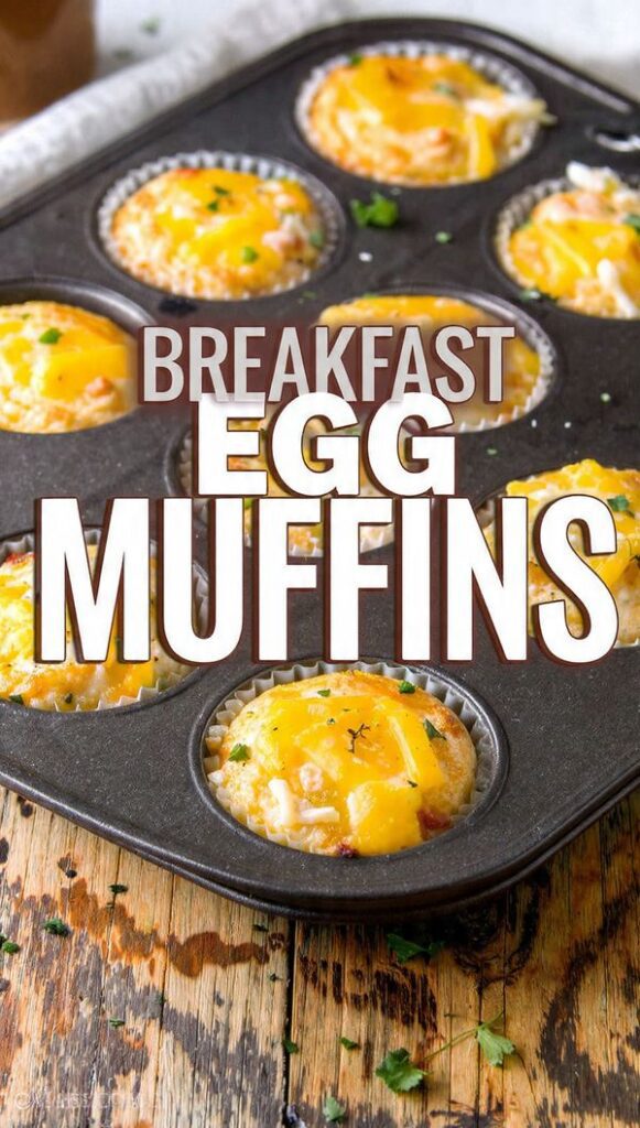 A close-up shot of a 12-cup muffin tin filled with golden-brown Breakfast Egg Muffins, some topped with melted cheese and visible bits of spinach and bacon. The text overlay reads: "BREAKFAST EGG MUFFINS".