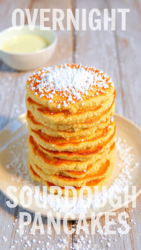 Close-up of a tall stack of fluffy sourdough pancakes with syrup dripping down, showing the texture