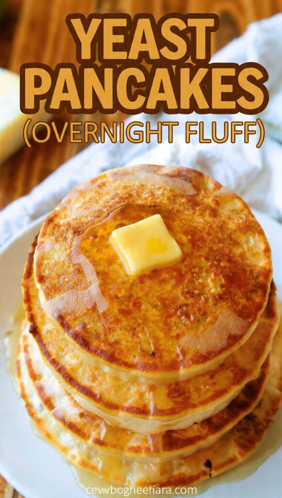 Close-up of a tall stack of fluffy yeast pancakes with a small pool of butter and syrup dripping.