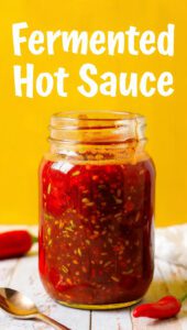 A bubbling glass jar of fermenting peppers and garlic with text overlay "Fermented Hot Sauce"
