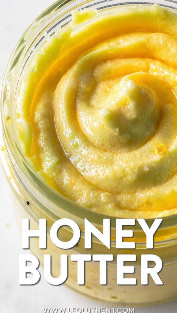 A glass jar of whipped honey butter with a wooden spreader and warm biscuits.