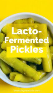 A glass jar of lacto-fermented pickles with dill and garlic and text overlay "Lacto-Fermented Pickles".
