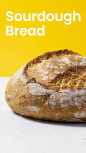 A crusty loaf of sourdough bread with a sharp ear and text overlay "Sourdough Bread From Starter"